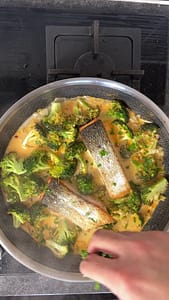 Hand sprinkling fresh chopped parsley over salmon and broccoli coconut curry.